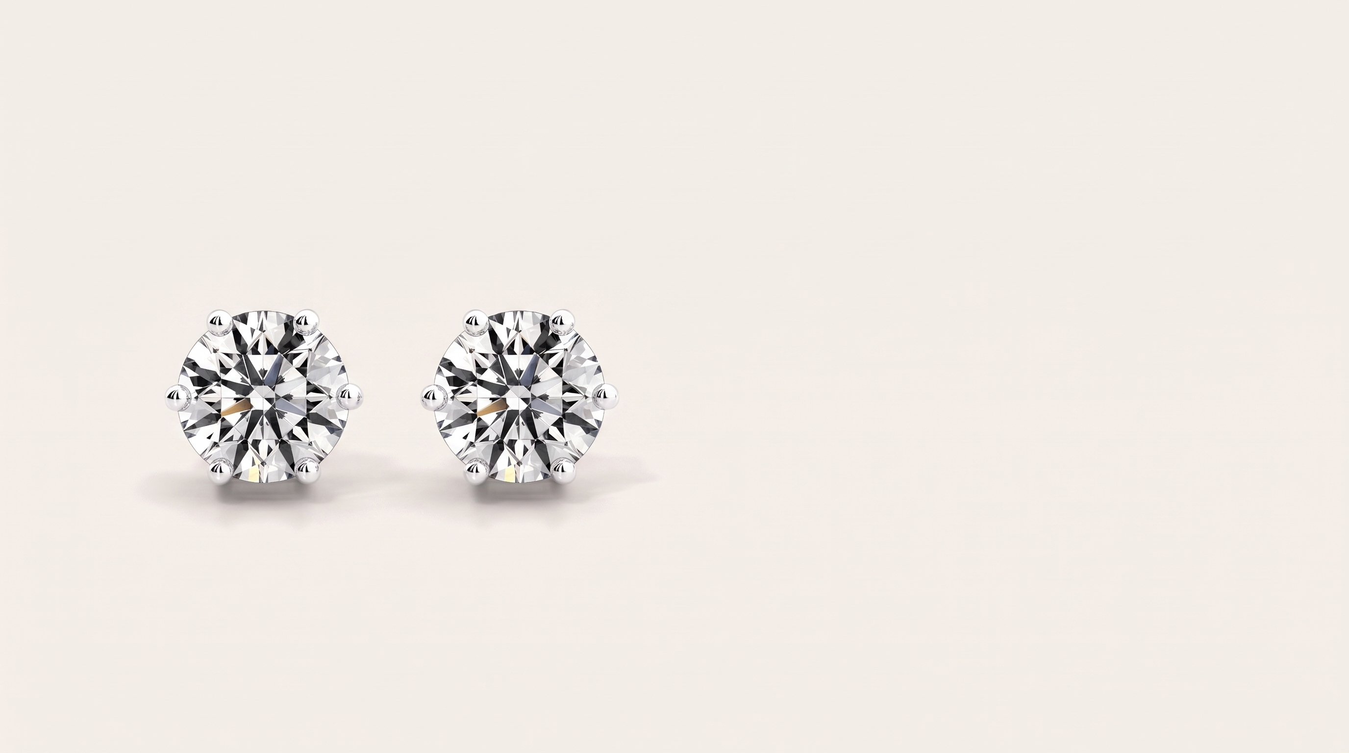 A pair of round six-prong silver stud earrings with large clear stones side by side on a warm off white background.