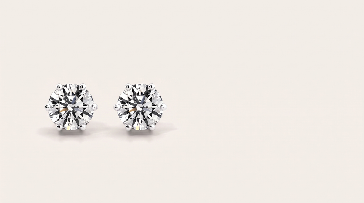 A pair of round six-prong silver stud earrings with large clear stones side by side on a warm off white background.