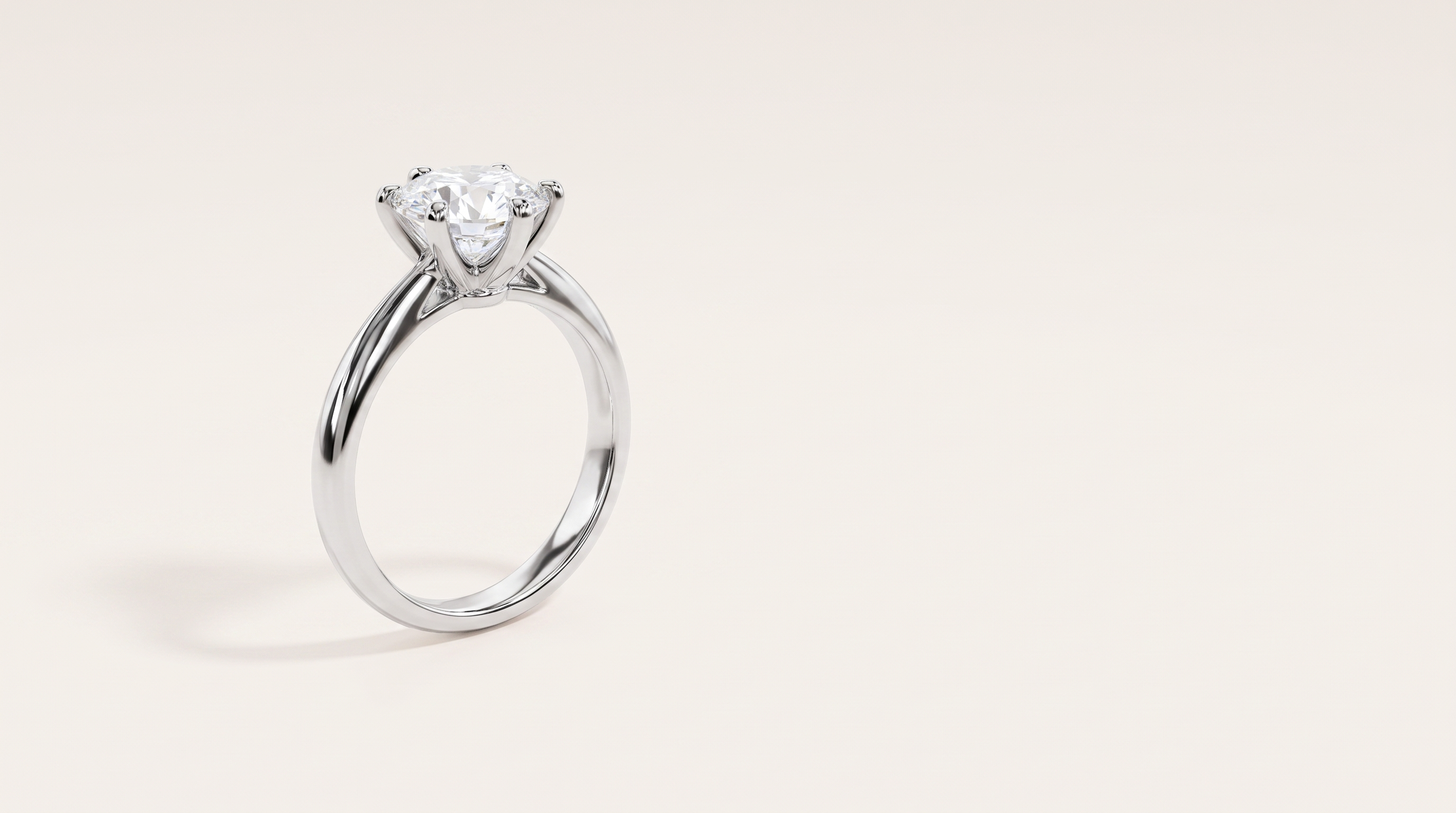 A silver six-prong solitaire ring with a round colourless stone, standing upright on a warm off white background.