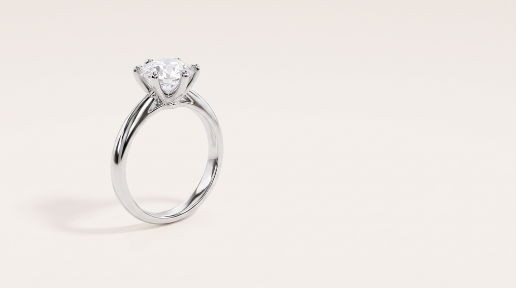 A silver six-prong solitaire ring with a round colourless stone, standing upright on a warm off white background.