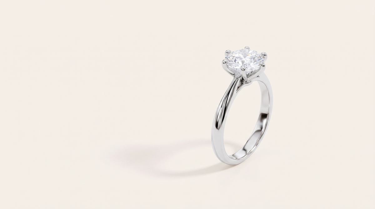A silver six-prong solitaire ring with one round, clear moissanite, standing on a warm off-white background in soft light.