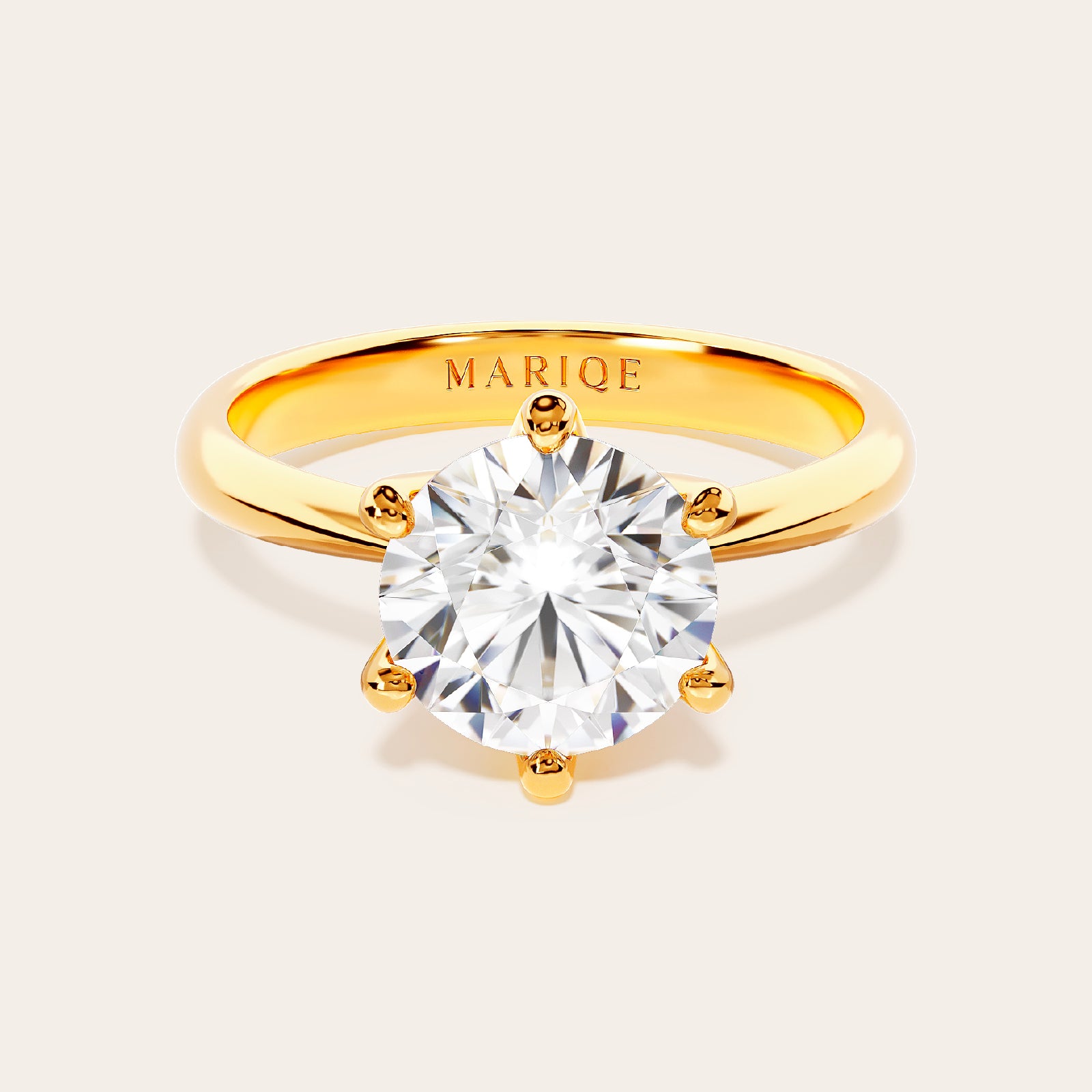 Gold ring with a large diamond on a light gray background, branded 'MARIQE'.